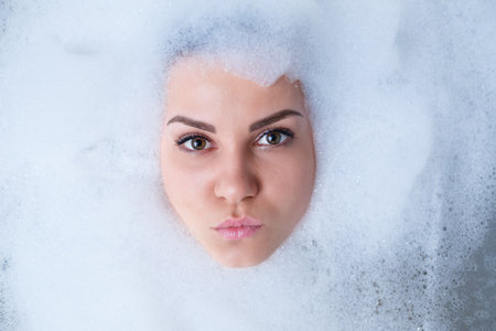 Closeup portrait of a girl in a bathtub and white foam around her face. Different emotions,...