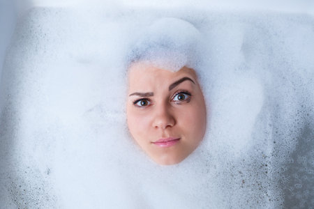 Closeup portrait of a girl in a bathtub and white foam around her face. Different emotions,...