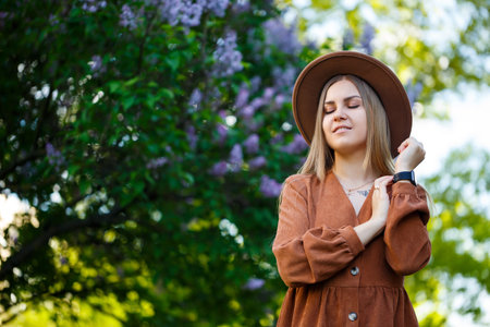 Portrait of a pretty girl in a brown hat with a lilac in the garden