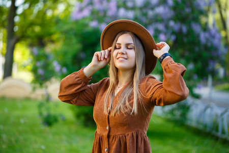 A beautiful girl with blond hair holds a hat in her hands and stands with her eyes closed near a...