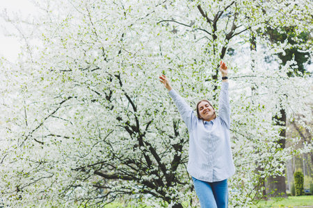 A woman in a white shirt and jeans with glasses in her hands in a spring garden.の写真素材