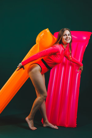 A slender young woman is dressed in a pink swimsuit, a smiling girl with air mattresses, isolated on...