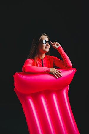 Young woman in a pink swimsuit, isolated on a dark background. Vacation lifestyle concept, summer...