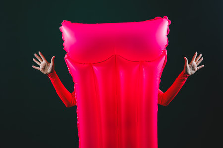 Pink inflatable mattress with female hands isolated on a dark background. Inflatable mattress for swimming on the waterの写真素材