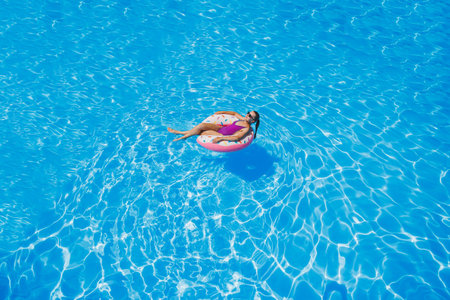Slim woman in sunglasses in the pool in an inflatable swimming ring in a bright swimsuit, summer...