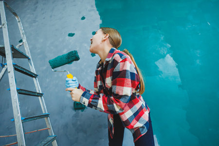 An emotional woman paints the walls. Young smiling pretty woman in shirt holding roller in right...