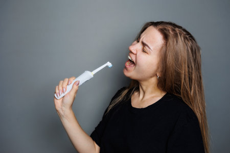 Portrait of a smiling young woman without makeup in a black t-shirt brushing her teeth, mature...