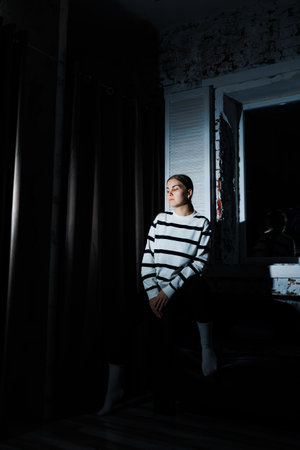 Cute stylish young woman in black leggings and striped jumper sitting on sofa. Women's fashion, women's casual style.の写真素材