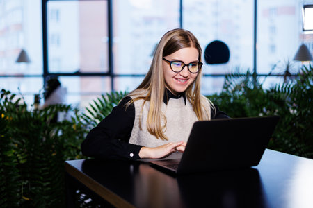 Beautiful smart attractive elegant woman businesswoman in a large company holds an online meeting with international business partners, she sits at a table at the workplace with a laptopの写真素材