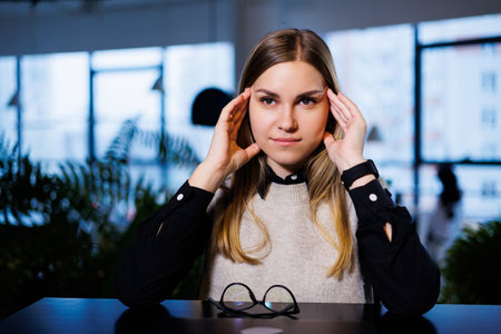 A young woman sits at a table with a closed laptop and massages her head from hard work and headaches. Woman suffering from migrainesの写真素材