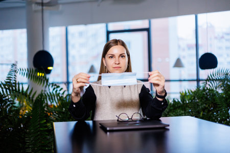 Beautiful young woman in a mask working in a cafe with a laptop during the coronavirus pandemic.の写真素材