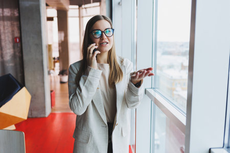 Young charming woman calling with a cell phone while sitting alone in a cafe in her free time, attractive woman with a sweet smile talking with a mobile phone while relaxing in a cafeの写真素材
