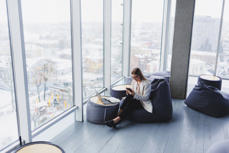 Focused female freelancer sitting in modern workspace with open netbook and checking notifications...