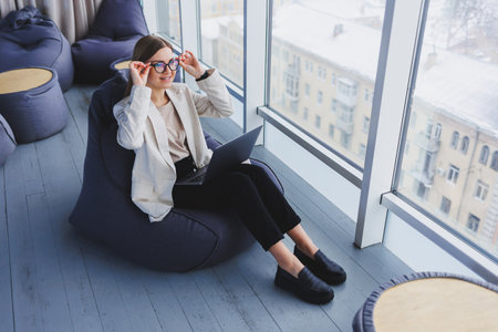 Successful woman in casual wear is typing on a netbook while working on a new project while sitting at a desk in a modern workspace. Business lady in a jacket and glasses. Teleworkの写真素材