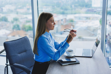 Beautiful business woman in a blue shirt sitting in the office with a laptop and doing business....