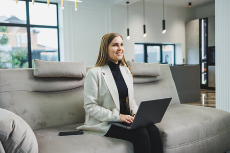 Woman cheerful charming person sitting behind a netbook watching having a good mood working at home indoors. Remote freelance workの写真素材