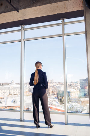 Confident business woman boss standing in modern office or hotel window enjoying big city view, woman leader, business owner thinking about future success, planning new opportunities,の写真素材