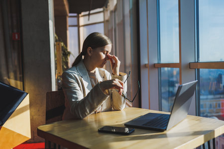 Young content worker in casual clothes sitting at a desk and using a netbook while working on the background of a spacious office. Business woman in the office works sitting near the windowの写真素材