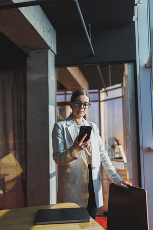 Cheerful young woman in casual wear having telephone conversation sitting at working place near laptop in office, smiling female freelancer calling to colleague for share good news about businessの写真素材