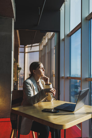Young content worker in casual clothes sitting at a desk and using a netbook while working on the background of a spacious office. Business woman in the office works sitting near the windowの写真素材