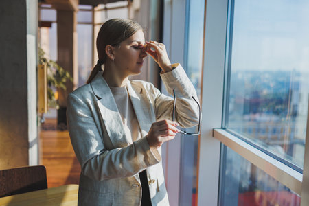 Headache in young business woman in casual clothes and glasses in office. Migraine from office work.の写真素材