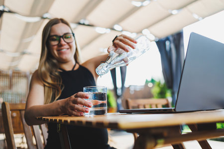 Female manager, freelancer, enjoying coffee break on summer terrace of cozy cafe, working remotely on laptop, smiling looking at laptop. Work online in the summerの写真素材