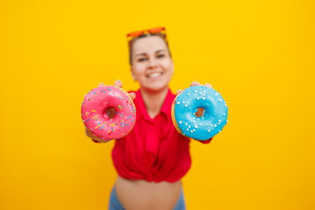 A bright pregnant woman in a pink shirt on a yellow background eats sweet donuts. Fresh sweet donuts in the hands of a pregnant womanの写真素材