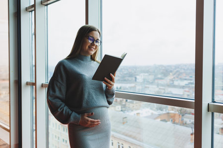Young pregnant woman at work in the office standing near the window. Work during pregnancy. Pregnant business ladyの写真素材