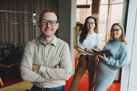 Young confident business people standing in an office space with a group of colleagues in the background, working on a laptop computer. The work of colleagues in a modern office.の写真素材