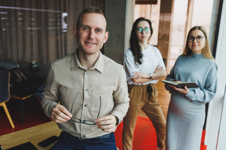 Young confident business people standing in an office space with a group of colleagues in the background, working on a laptop computer. The work of colleagues in a modern office.の写真素材