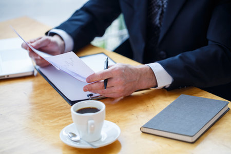 Adult male mentor, director, businessman in glasses and a suit studying documents while sitting at the table. Working day conceptの写真素材