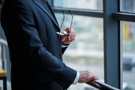 Adult male businessman, teacher, mentor looks out the large window of his office. Work in the office. Development of a new business projectの写真素材