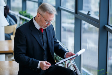 Man managing director leaned on a wooden table in his office near a large window and looks at a successful business development plan.の写真素材