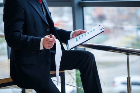 Man managing director leaned on a wooden table in his office near a large window and looks at a successful business development plan.の写真素材
