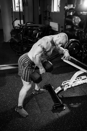 Muscular shirtless man doing dumbbell exercises as part of his bodybuilding workout. Fitness motivation, sports lifestyle, health, athletic body, body positiveの写真素材