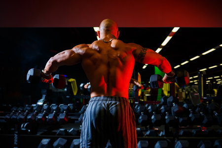 Muscular shirtless man doing dumbbell exercises as part of his bodybuilding workout. Fitness motivation, sports lifestyle, health, athletic body, body positiveの写真素材