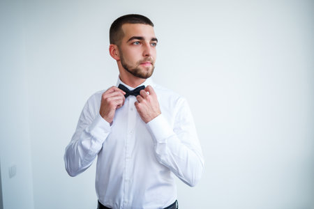 Young male businessman dressed in a white shirt with a short beard wears a black bow tieの写真素材