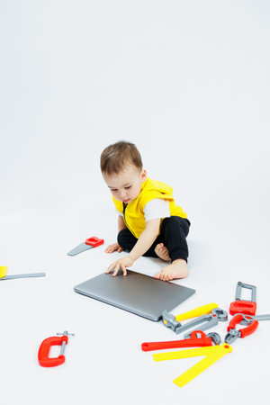 A cute 2-year-old boy is sitting at a digital laptop on a white background. Child and modern...