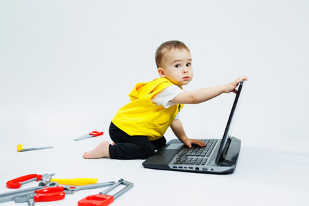 A cute 2-year-old boy is sitting at a digital laptop on a white background. Child and modern...