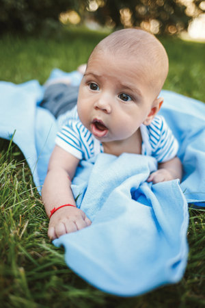 Little boy 3 months old lies on his stomach on a blue bedspread in the park around the green grass...