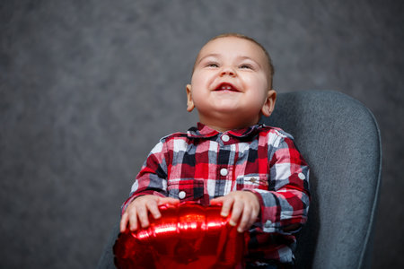 A little boy in a shirt plays with a balloon in the form of a heartの写真素材