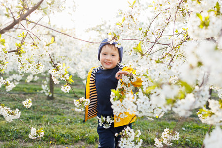 A little three-year-old joyful boy runs on the grass in a blooming garden in the spring. Children emoticon of joy, happy smiling child.の写真素材