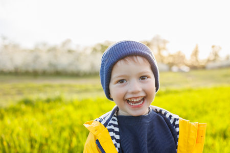 A cute little three-year-old boy in a yellow jacket and cap is running on a green field. A smiling child runs on green grassの写真素材