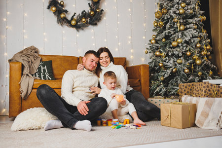 A happy young family with a small child is celebrating the New Year at home near the Christmas tree....