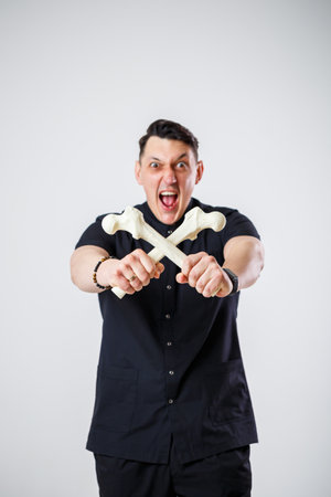 Young male doctor chief physician in a black surgical suit. Close-up portrait. Holds a femur in his hands. Isolated on white background.の写真素材