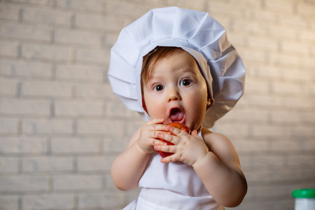 Little boy dressed as a cook in the kitchen. Handsome child dressed in an apron eating an appleの写真素材