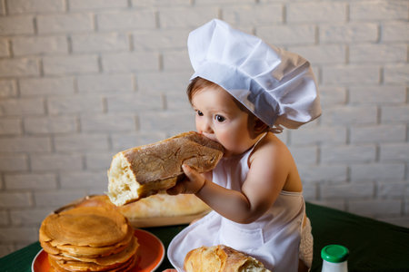 Little boy dressed as a cook in the kitchen. Handsome child dressed in an apron eating breadの写真素材