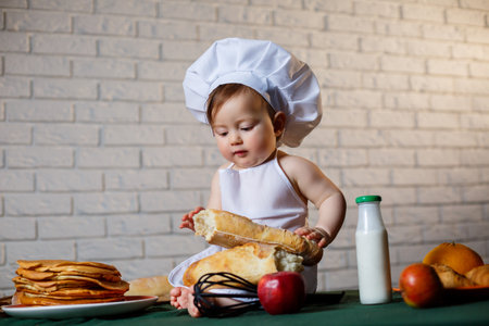 Little boy dressed as a cook in the kitchen. Handsome child dressed in an apron eating breadの写真素材