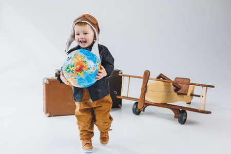 A boy in a leather jacket and a pilot's hat, a wooden plane, a globe, brown suitcases. Children's wooden toysの写真素材