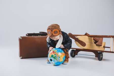 A boy in a leather jacket and a pilot's hat, a wooden plane, a globe, brown suitcases. Children's wooden toysの写真素材